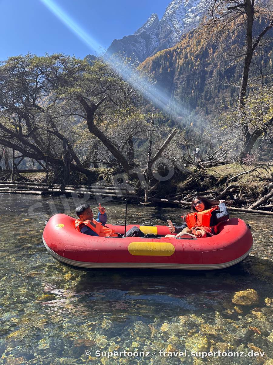 นั่งเรือยางสีแดงในลำธารน้ำใส มีภูเขาหิมะเป็นฉากหลัง